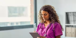 Healthare professional in scrubs looks at their tablet 