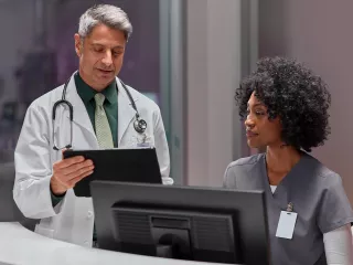 Two clinicians look at data on a desktop and tablet device.