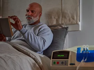 A man reads in bed next to the Homechoice Claris APD System
